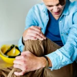 Wypadek przy pracy pracownik trzymający się za nogę w wyniku upadku