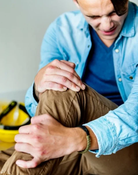 Wypadek przy pracy pracownik trzymający się za nogę w wyniku upadku