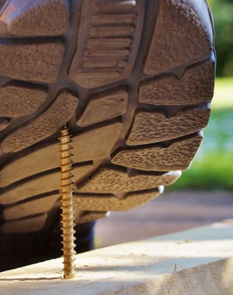 Pracownik stąpający butem na wystający gwóźdź